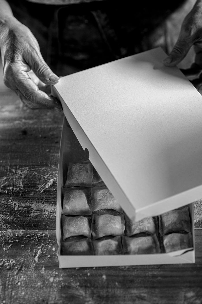 services-05 Black and white image showing hands packing homemade pastries into a box, emphasizing craftsmanship.