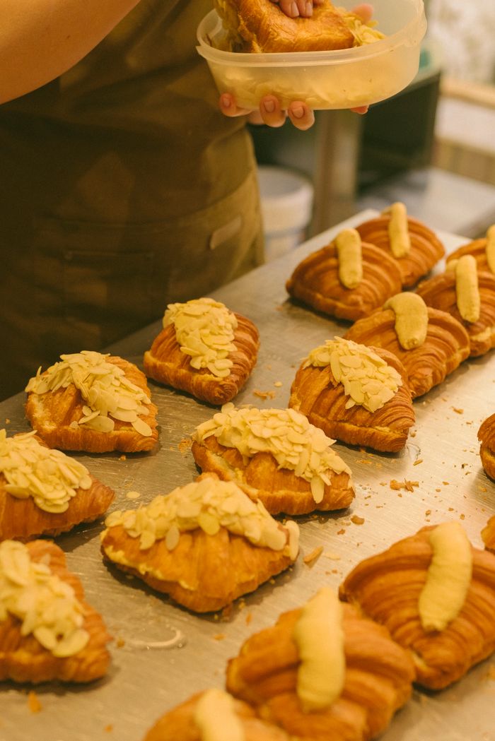 services-09 Close-up of fresh almond croissants being prepared by a bakery chef.