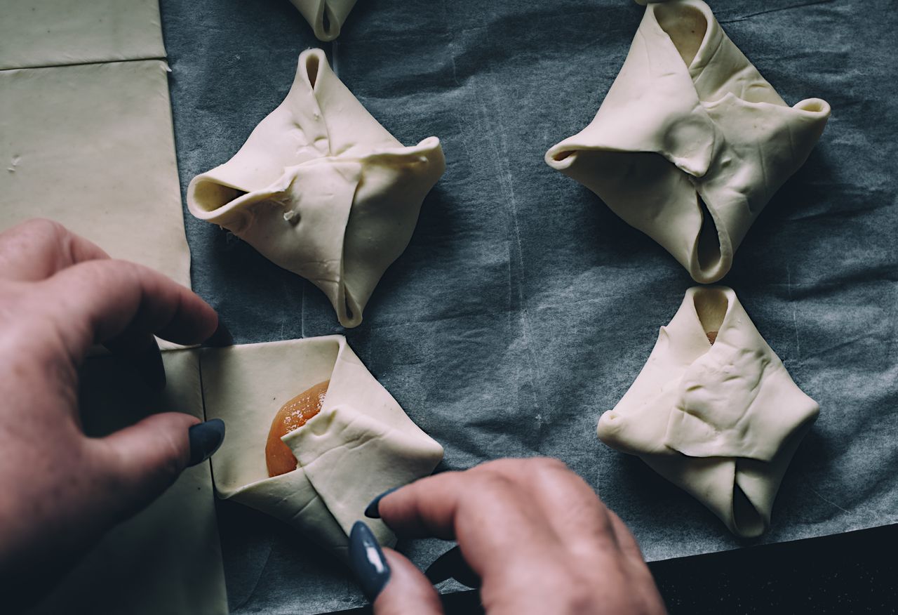 our-mission Close-up of hands folding pastry parcels on parchment paper in a kitchen setting.