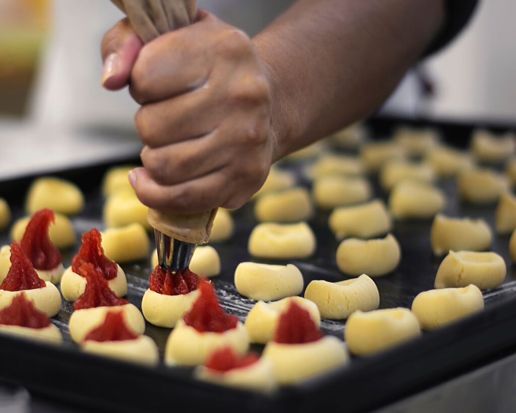 The Art of Drawing Readers In: Your attractive post title goes here Close-up of a baker using a piping bag to fill pastries with jam, showcasing the preparation process.